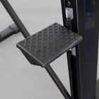 Black metal step platform attached to a piece of exercise equipment on a light gray background