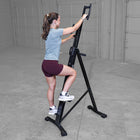 Woman using climber machine in a room with gray flooring and walls.