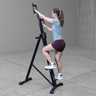 Woman using a home gym machine in a room with gray walls and floor.