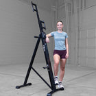 A woman in athletic wear stands next to a large black A-frame wall climbing exercise machine in a spacious concrete garage or warehouse setting.