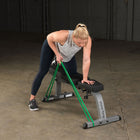 Woman exercising with a resistance band on an adjustable weight bench in a garage setting.