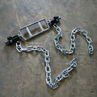 A silver metal chain with a rectangular barbell handle and black weight plates, laid out on a textured brown surface.