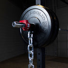 A close-up of a barbell with a large black 45 lb BODY-SOLID weight plate, a red weight pin protector, and a hanging silver chain in a dark gym setting.