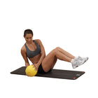 Woman exercising with a yellow ball on a black mat against a white background