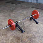 A barbell with red weight plates resting on a black adjustable weight bench in a concrete gym floor setting.
