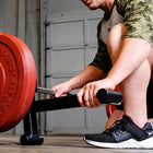 A person in a gym setting using a black weight bench press with a barbell and red weight plates. 
