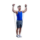 A man wearing a blue tank top and gray shorts exercises with a resistance band against a solid white background.