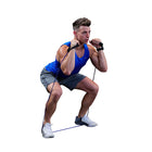 A man in a blue tank top and gray shorts performing a squat while using a blue resistance band with black handles on a solid white background.