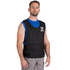A man wearing a black weight vest over a blue shirt and gray pants, standing against a plain white background.