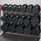 A rack of black rubber-coated dumbbells with silver metal handles, arranged in three rows on a white rack in a gym setting.