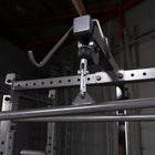 A close-up of a silver metal weight rack accessory with a hook and adjustable clamp mechanism attached to a steel frame in an industrial gym setting.
