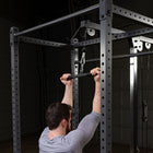 A man in a gray long-sleeve shirt uses a cable pulley exercise machine on a black metal power rack in a dark garage.