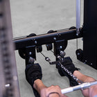 Close-up of a person using a cable pulley exercise machine in a gym, with their feet resting on footrests and hands pulling a bar with a chain attachment.