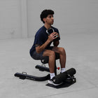 Person using a black exercise machine in a minimalistic room