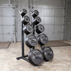 A black metal weight rack holding multiple black weight plates with white text, photographed in a garage-like indoor space with gray doors and concrete floor.