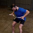 A man in a blue athletic shirt and black shorts performing a cable pull-through exercise in a gym with concrete floors.