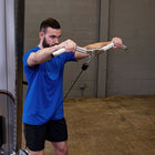 A man in a blue t-shirt and black shorts performing a cable pull-through exercise with a silver cable pulley system in a gym setting.