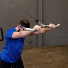A man in a blue t-shirt performing a cable pull-through exercise in a gym with a gray brick wall background.