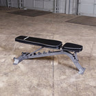 A silver adjustable weight bench with black padded foam surfaces, photographed on a concrete warehouse floor.