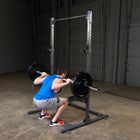 Person performing squats with a barbell on a squat rack in a gym setting