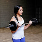 A woman in a gym setting performing a bent-over barbell curl. 